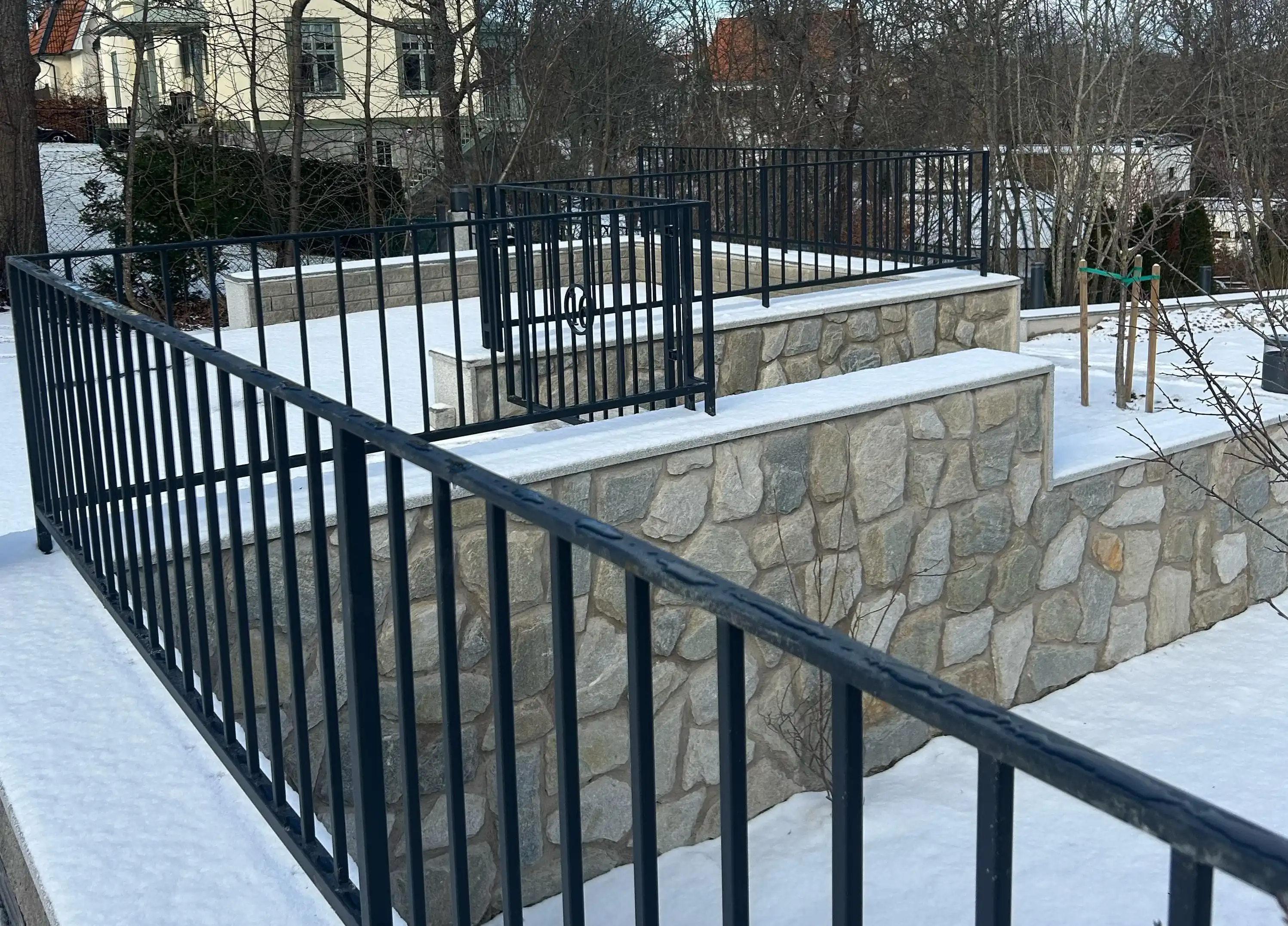 Bilden visar en vackert utformad stenmur med trappor, omgiven av ett svart metallräcke, i ett snöigt landskap. Stenläggningen är snygg och estetiskt tilltalande, vilket skapar en stilfull och hållbar gräns. Designen är elegant, med en kombination av naturlig sten och modern metallstängsel, perfekt för att förbättra utseendet på bostadens utomhusområden. Detta kan vara ett utmärkt exempel på professionellt stenarbete och landskapsdesign för SEO, som lyfter fram kvaliteten och skönheten i stenbyggnation i bostadsområden. Bilden visar en vackert utformad stenmur med trappor, omgiven av ett svart metallräcke, i ett snöigt landskap. Stenläggningen är snygg och estetiskt tilltalande, vilket skapar en stilfull och hållbar gräns. Designen är elegant, med en kombination av naturlig sten och modern metallstängsel, perfekt för att förbättra utseendet på bostadens utomhusområden. Detta kan vara ett utmärkt exempel på professionellt stenarbete och landskapsdesign för SEO, som lyfter fram kvaliteten och skönheten i stenbyggnation i bostadsområden.